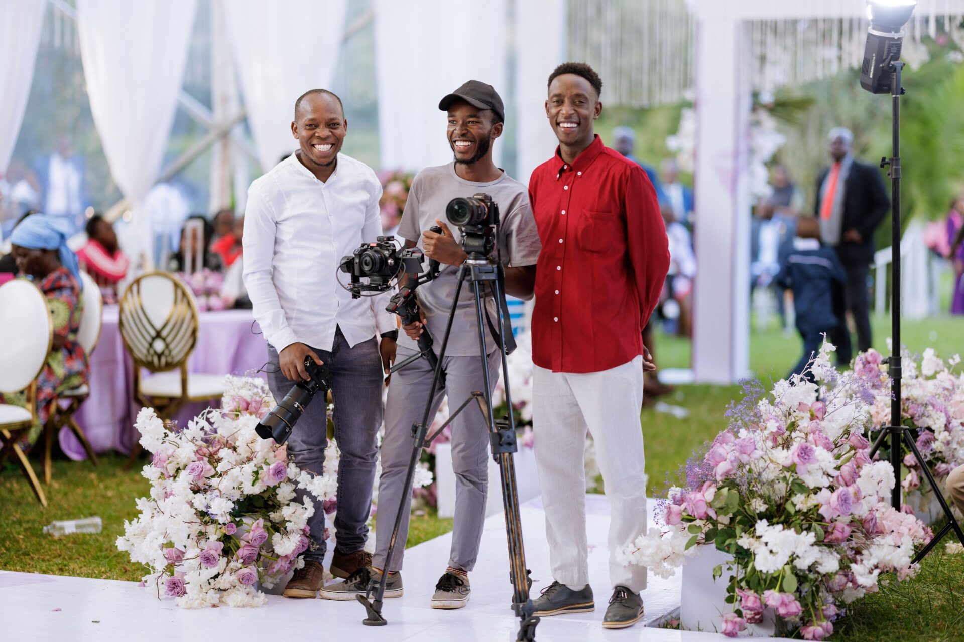 A group of camera men at an ornate event surrounded by flowers smiling for the camera