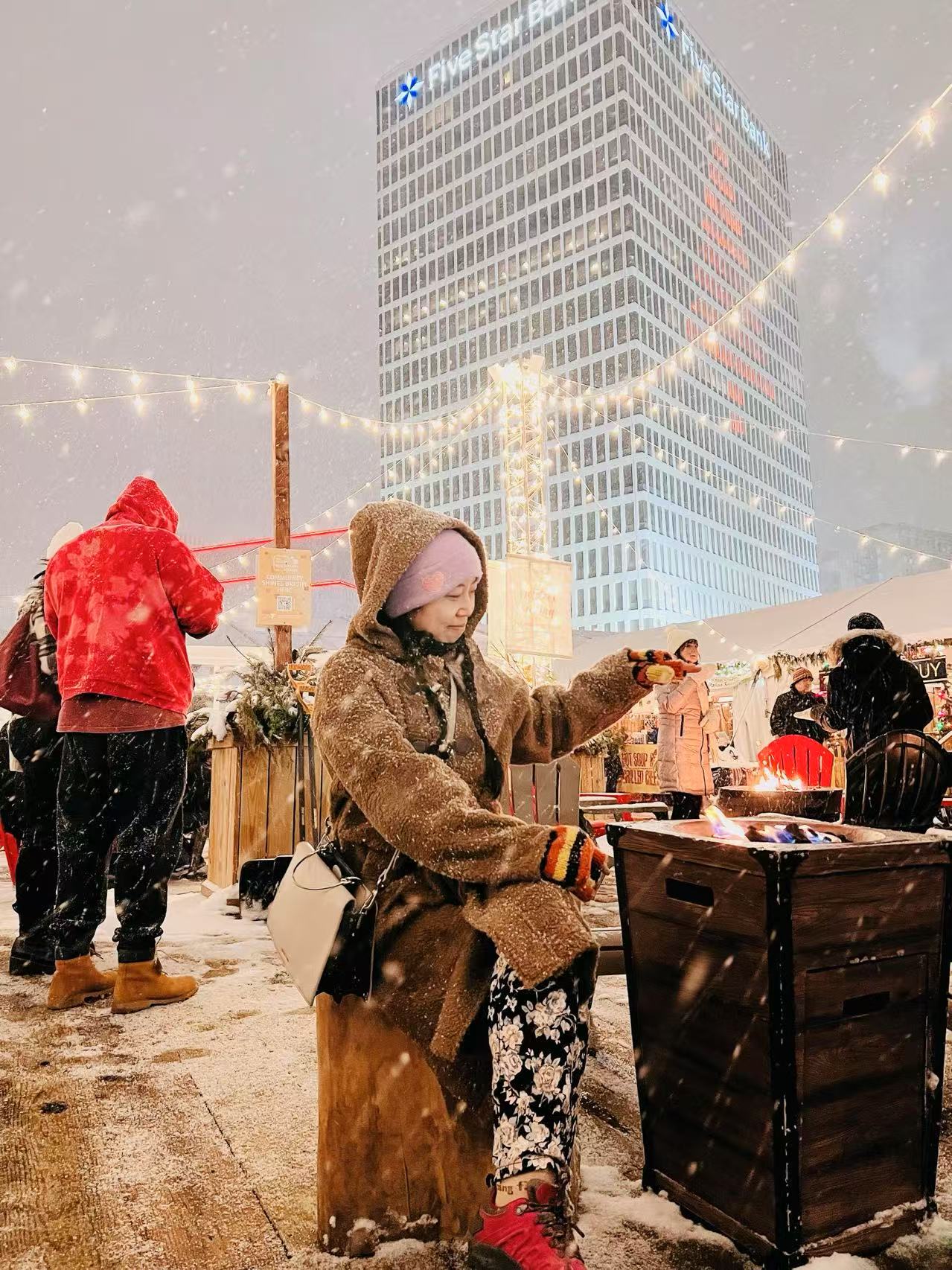 A snowy city rooftop bar with a student sitting in front of a portable fireplace