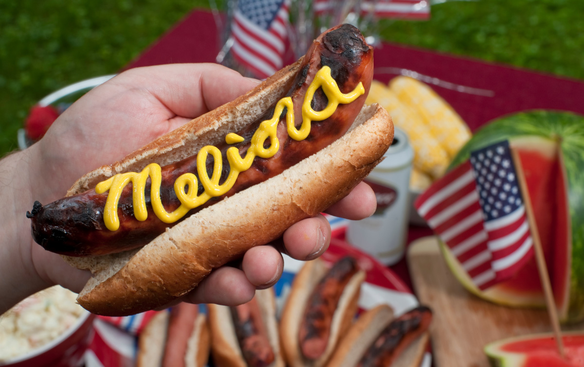 At a summer picnic, the word Meliora is written out on a hotdog using mustard.