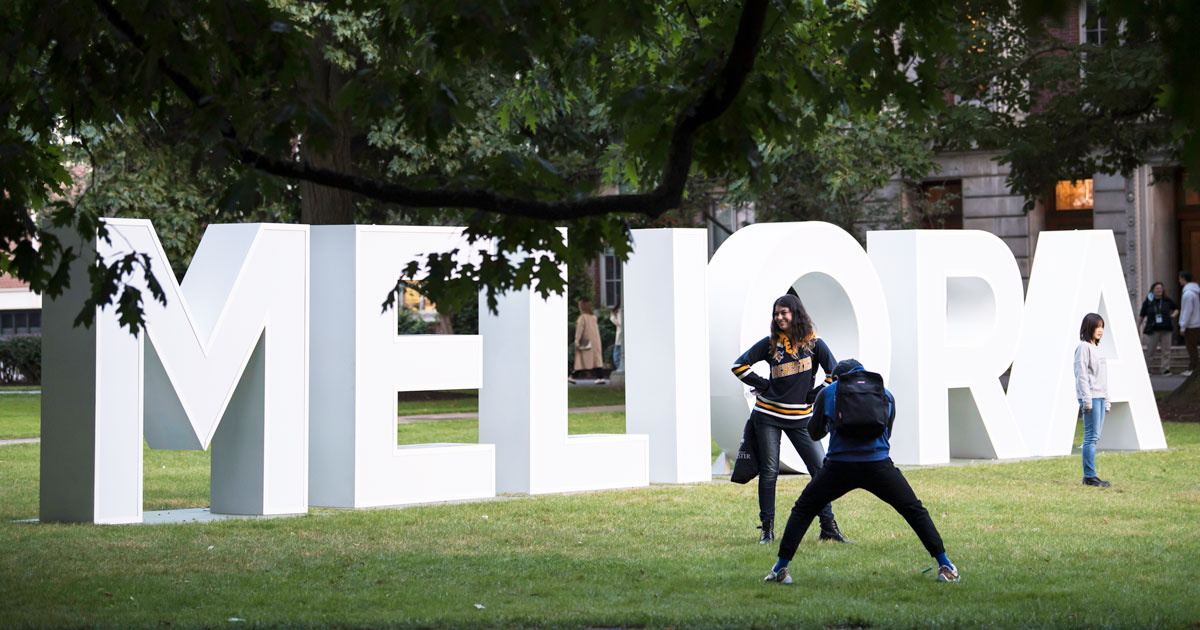 Students pose in front of the Meliora letters on the University of Rochester campus