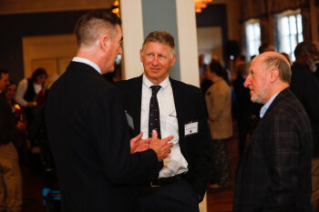 A candid photo of three men conversing at the George Eastman Circle Faculty & Staff Reception held on March 30, 2023 within Rochester New York.