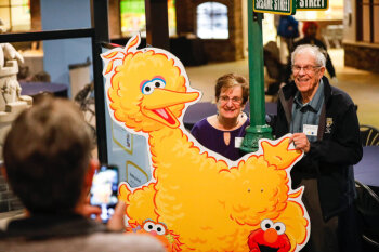 A couple pose in front of a poster with characters from Sesame Street at the George Eastman Circle Family Celebration, held on April 27, 2023 within Rochester New York.