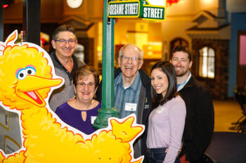 COVER photo A group of five people pose in front of a poster of big bird at the A couple pose in front of a poster with characters from Sesame Street at the George Eastman Circle Family Celebration, held on April 27, 2023 within Rochester New York.