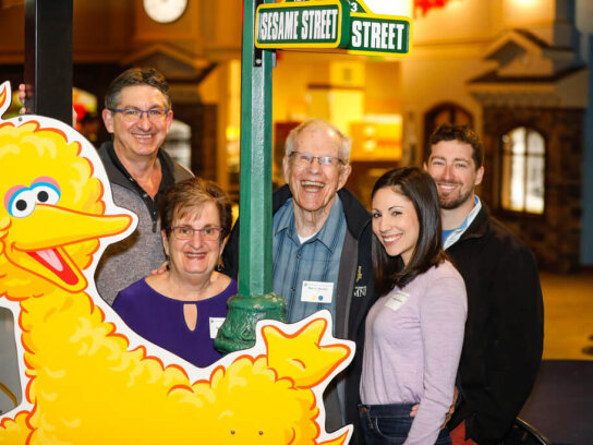 COVER photo A group of five people pose in front of a poster of big bird at the A couple pose in front of a poster with characters from Sesame Street at the George Eastman Circle Family Celebration, held on April 27, 2023 within Rochester New York.