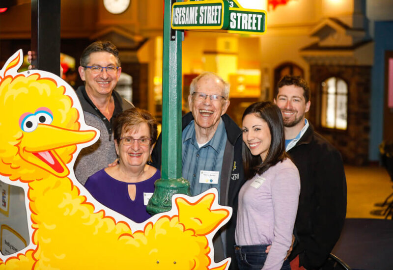 COVER photo A group of five people pose in front of a poster of big bird at the A couple pose in front of a poster with characters from Sesame Street at the George Eastman Circle Family Celebration, held on April 27, 2023 within Rochester New York.