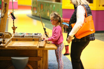 A girl in front of a desk with a woman behind her