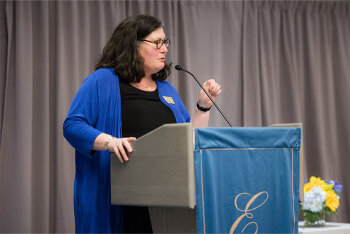 A woman at lectern on stage speaking