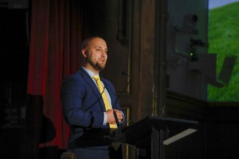 A man on stage speaking at a lecturn