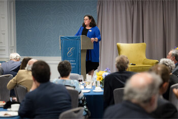 People watching a woman on stage speaking at the lectern