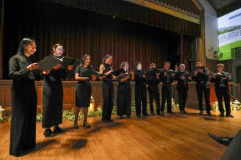 A choir standing in front of a stage dressed in black performing