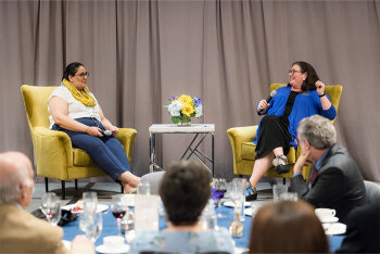 People watching 2 women seated on stage speaking