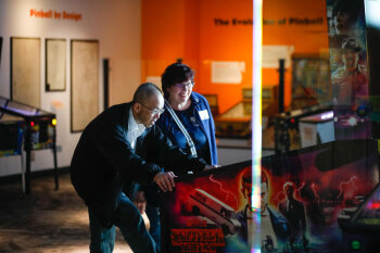 A candid photo of a man and woman playing the stranger things pinball game at the George Eastman Circle Family Celebration, held on April 27, 2023 within Rochester New York.