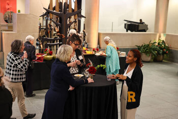 three Attendees have a conversation at a table, while four other attendees select food from another table