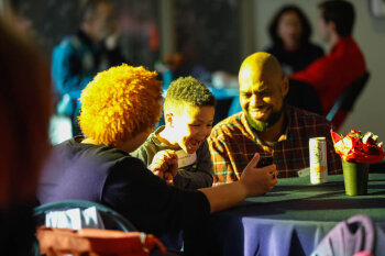 A candid photo of a child whom appears extremely excited as they are being shown something on a phone, as a man and woman watch in delight at the George Eastman Circle Family Celebration, held on April 27, 2023 within Rochester New York.