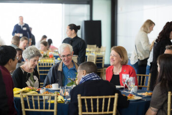 A candid group photo of seven eating and conversing at the George Eastman Circle Family Celebration, held April 30, 2023, within Washington, DC.