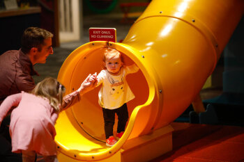 A man helps a young toddler out from a yellow slide at the George Eastman Circle Family Celebration, held on April 27, 2023 within Rochester New York.