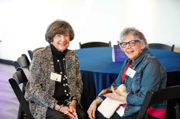 Two women sit and smile at a round table during the George Eastman Circle Faculty & Staff Reception in Rochester.