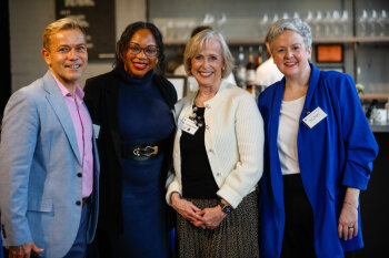 Four guests stand together and pose for a group photo near the bar area at the George Eastman Circle Faculty & Staff Reception on March 19, 2025.
