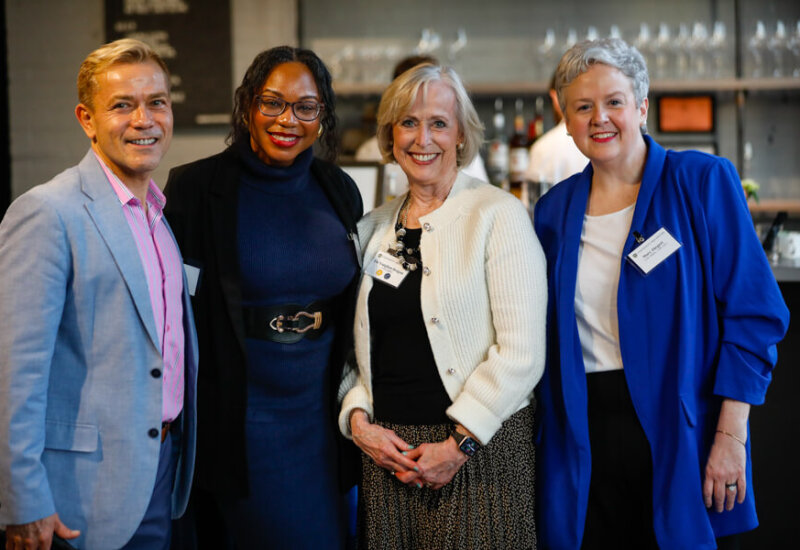 Four guests stand together and pose for a group photo near the bar area at the George Eastman Circle Faculty & Staff Reception on March 19, 2025.