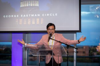 A guy on stage speaking into a mic on a glass lecturn