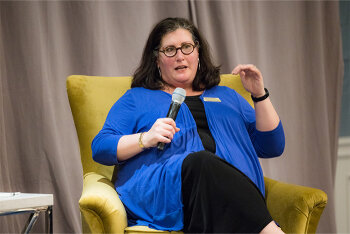 A woman seated on stage speaking