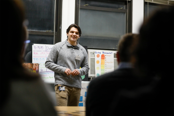 A man speaking with people's backs towards the camera