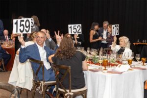 guests seated at tables hold up their auction numbers to bid