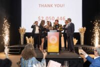 leaders pose on stage with glasses of champagne celebrating total money raised