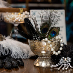A peacock feather, fake pearls, and feathers with gloves on table