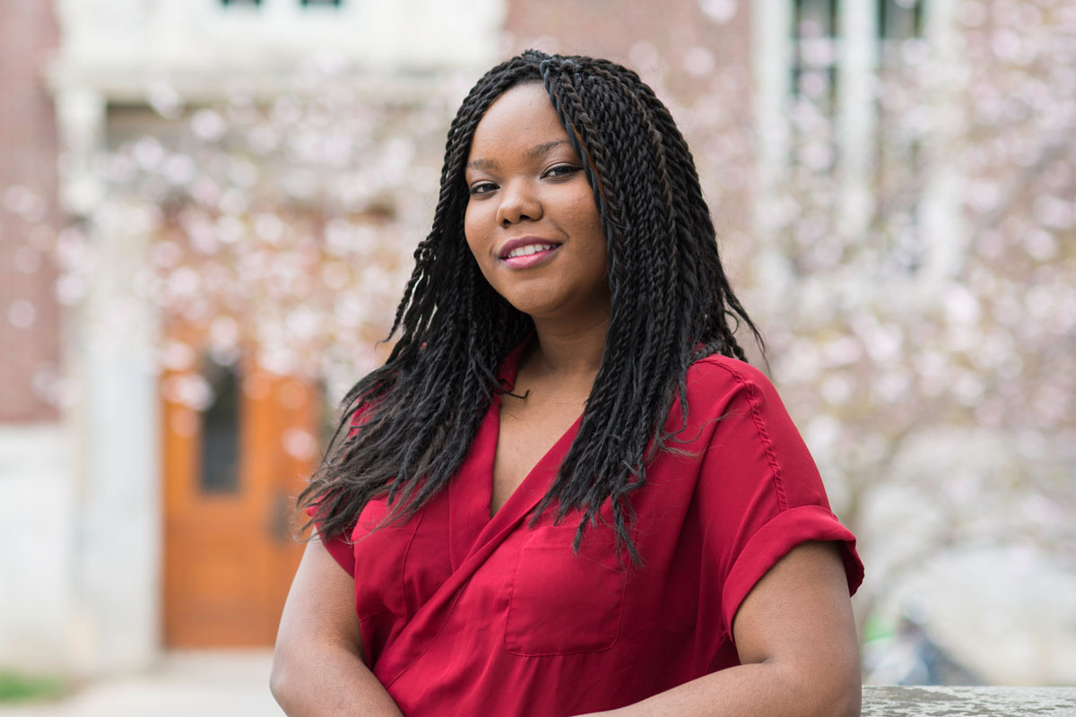 A University of Rochester student with dreadlocks sits on a bench, looking thoughtfully into the distance.