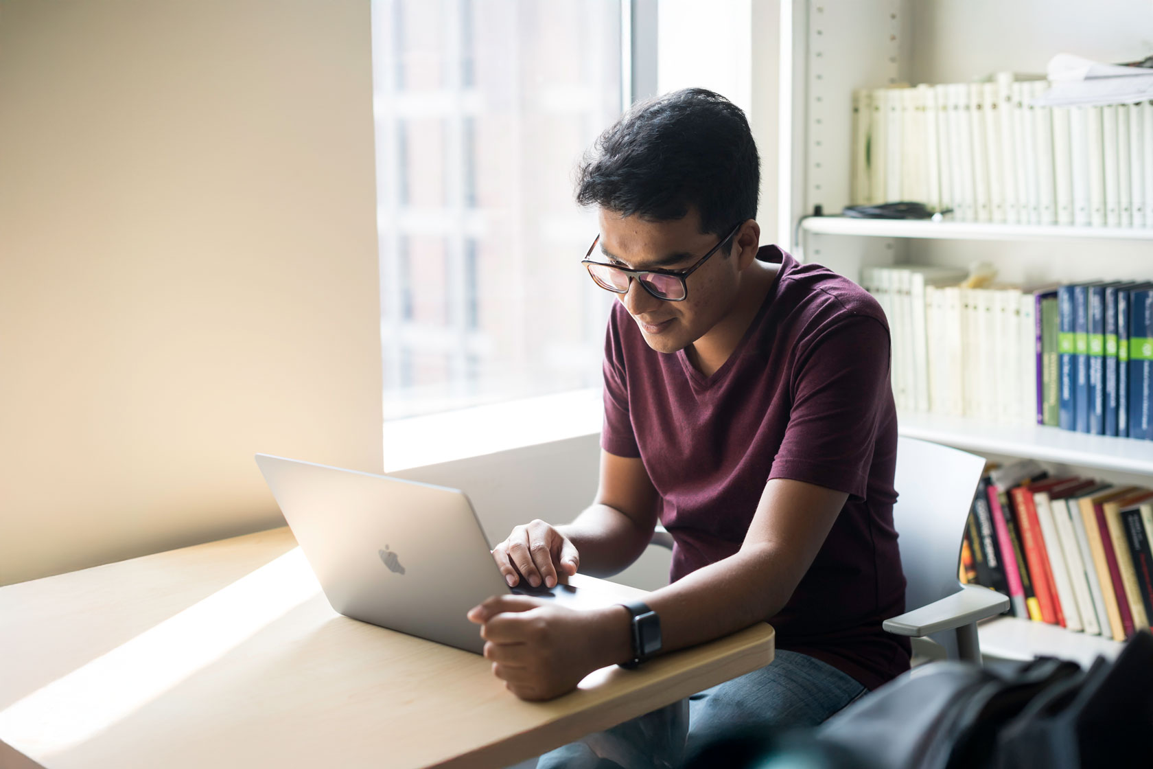 A University of Rochester student sitting at a desk, focused on his laptop while studying.