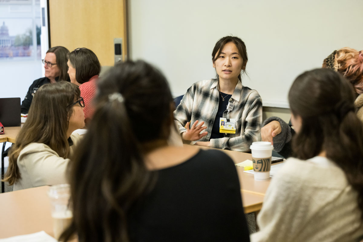 A group of University of Rochester students engaged in discussion around a table in a classroom setting.