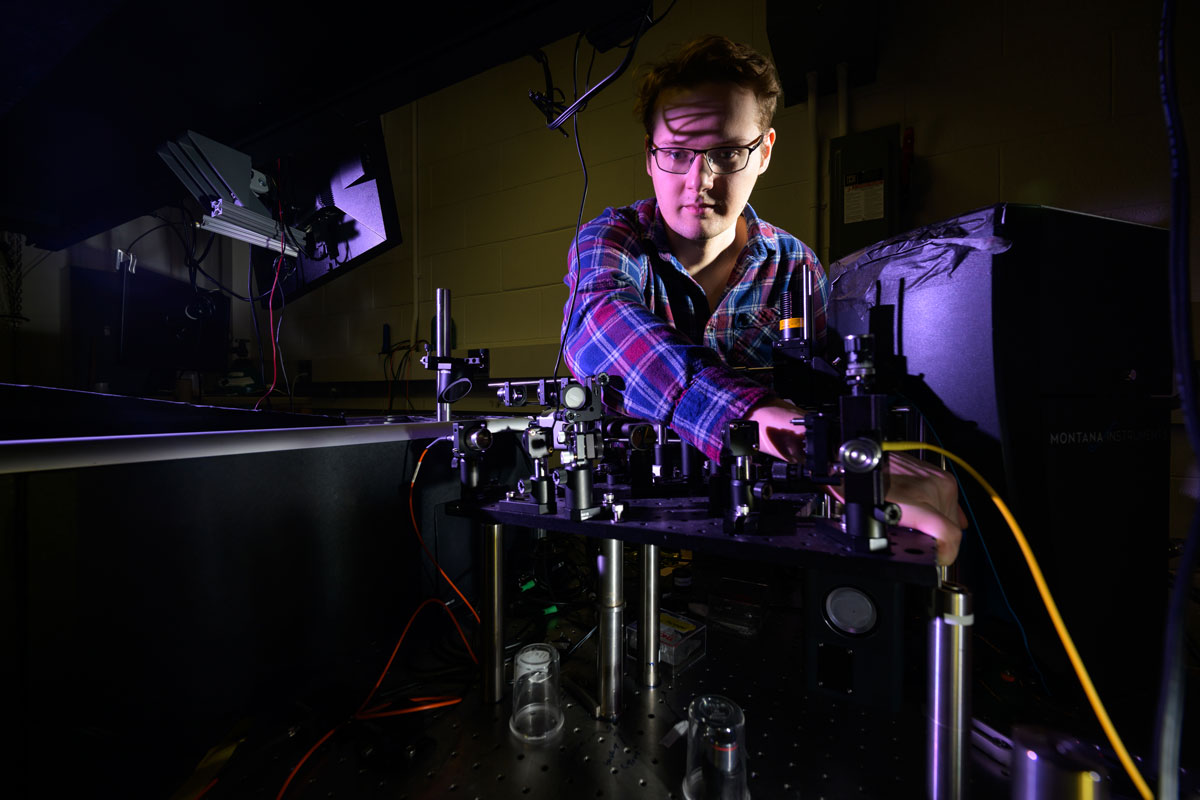 A University of Rochester student examines a sample under a microscope in a laboratory setting.