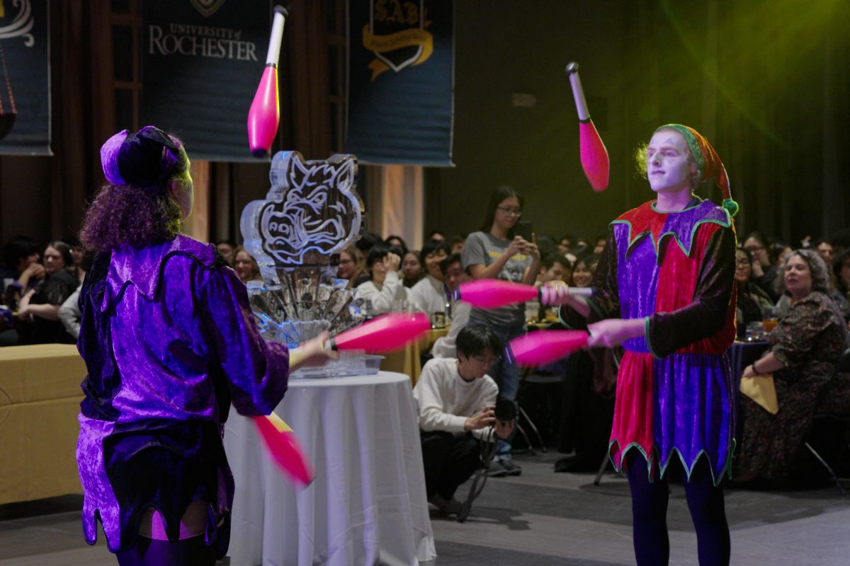 Two people in costumes juggling pink balls at the University of Rochester Boar's Head Dinner event.