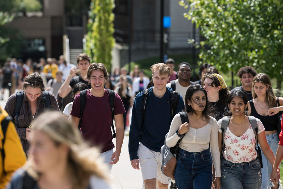 A group of University of Rochester students walking together on a campus sidewalk.