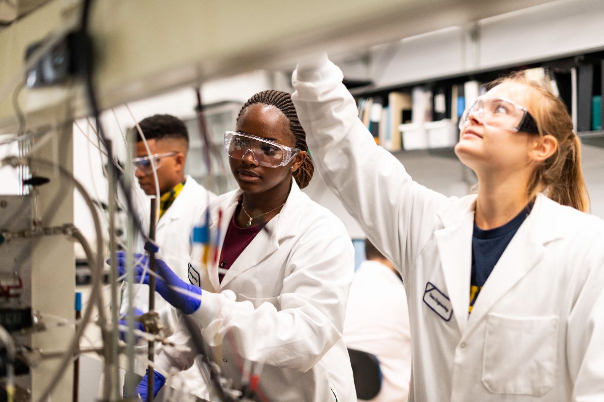 Two University of Rochester students in lab coats collaborate on a machine in a laboratory setting.
