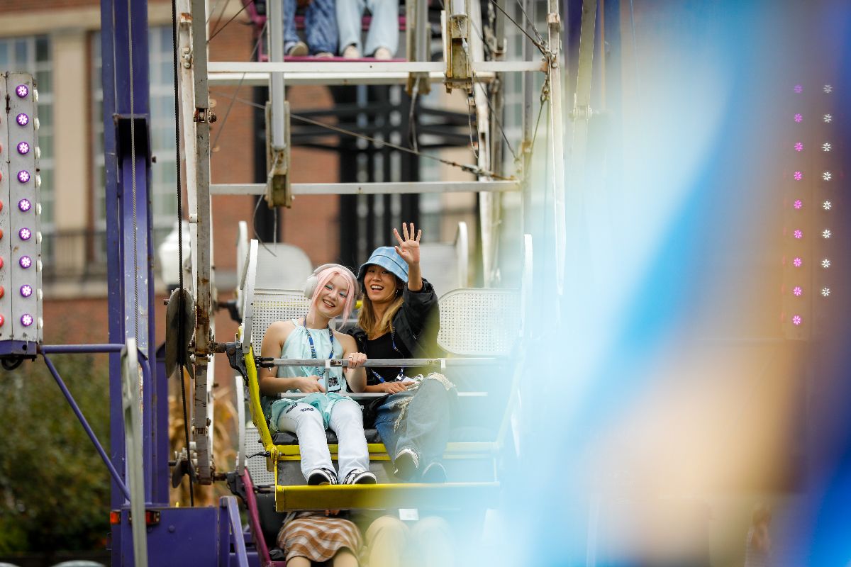 Two University of Rochester students enjoy a ride together on a colorful ferris wheel against a clear blue sky.