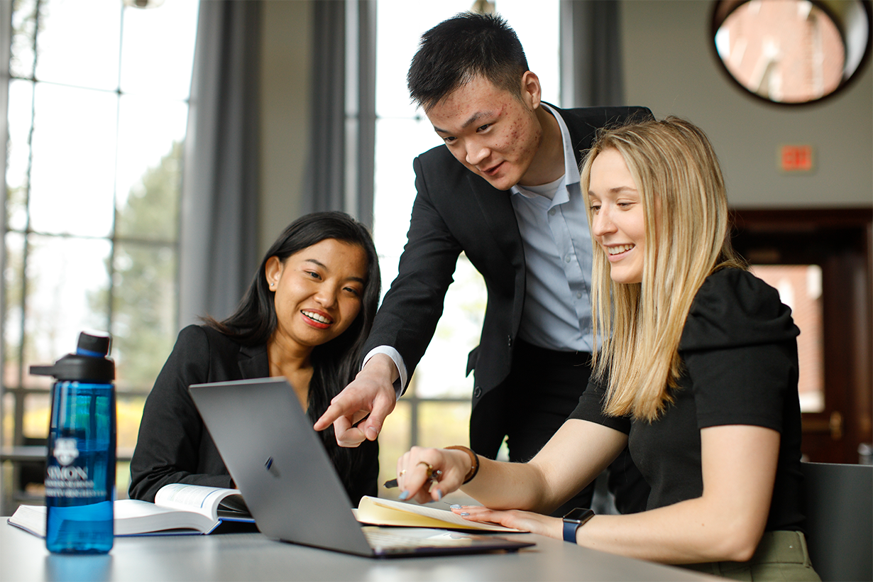Three business students look at a computer together.