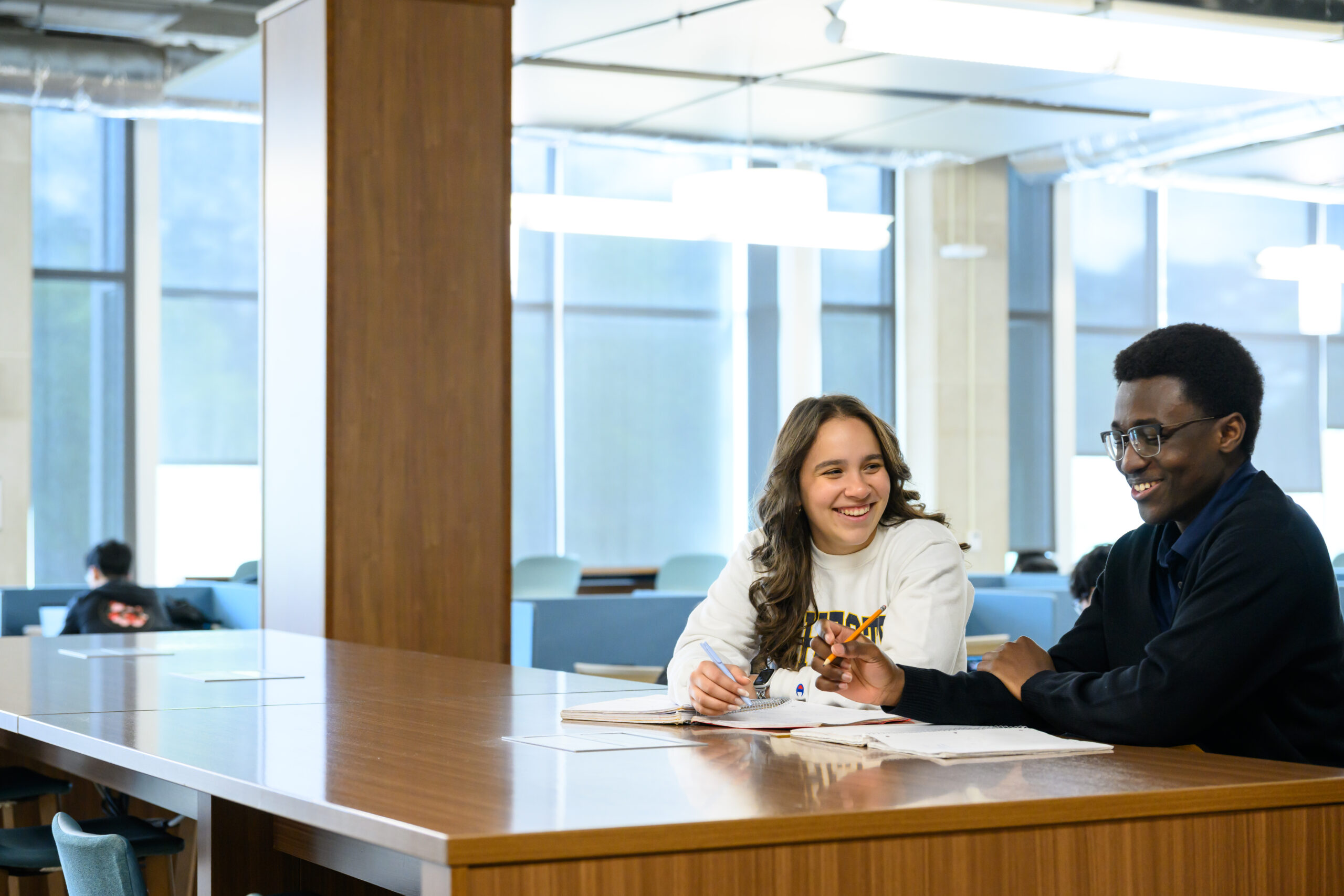 Two students sit at a table smiling work in Rush Rhees Library’s Gleason Library.