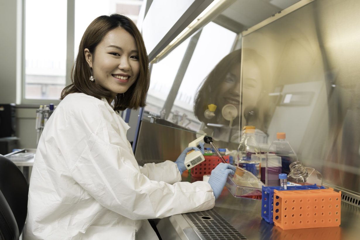 University of Rochester PhD candidate wearing gloves and a lab coat doing research