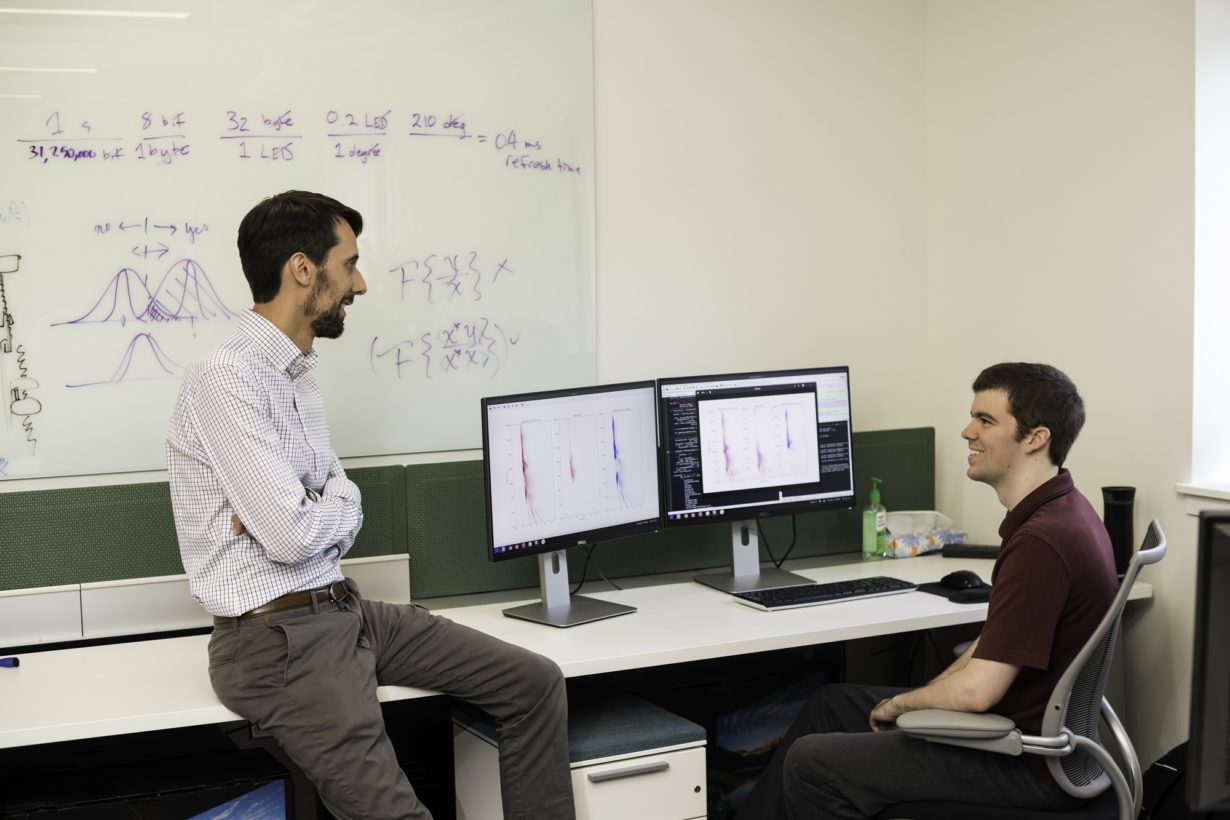 A graduate student and professor in a computer lab discussing charts that are displayed on a computer.