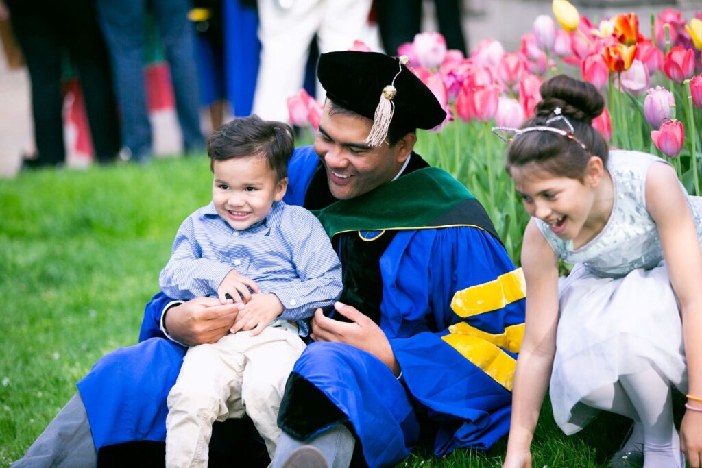 A University of Rochester graduate in full regalia, celebrating with his young children