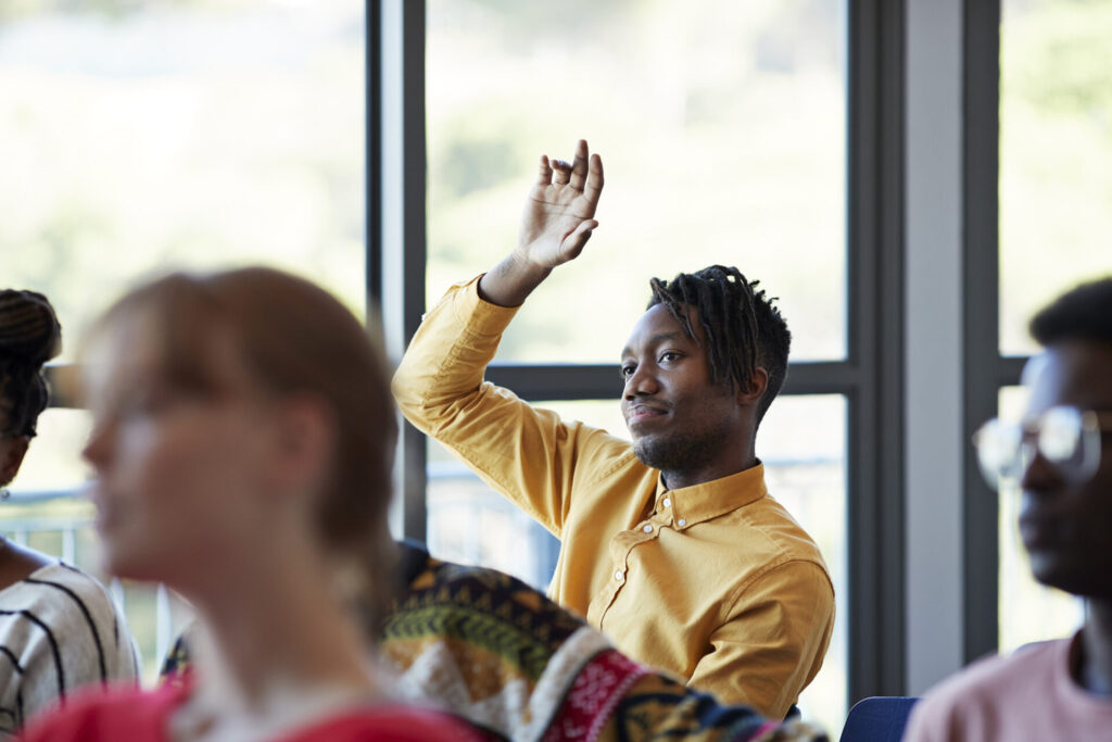 A student raises his hand in a lecture hall