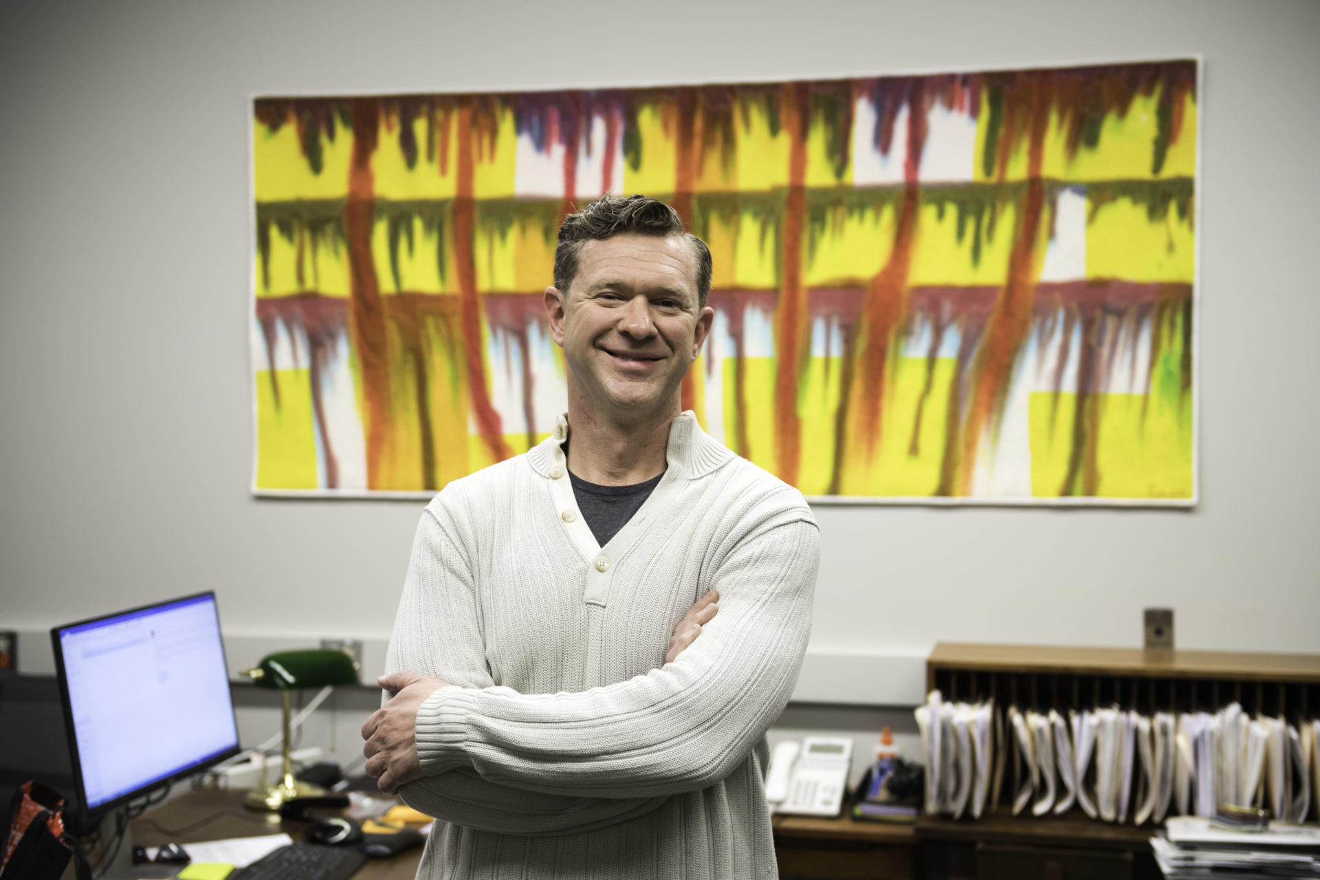 University of Rochester employee poses at his desk with quilts he created