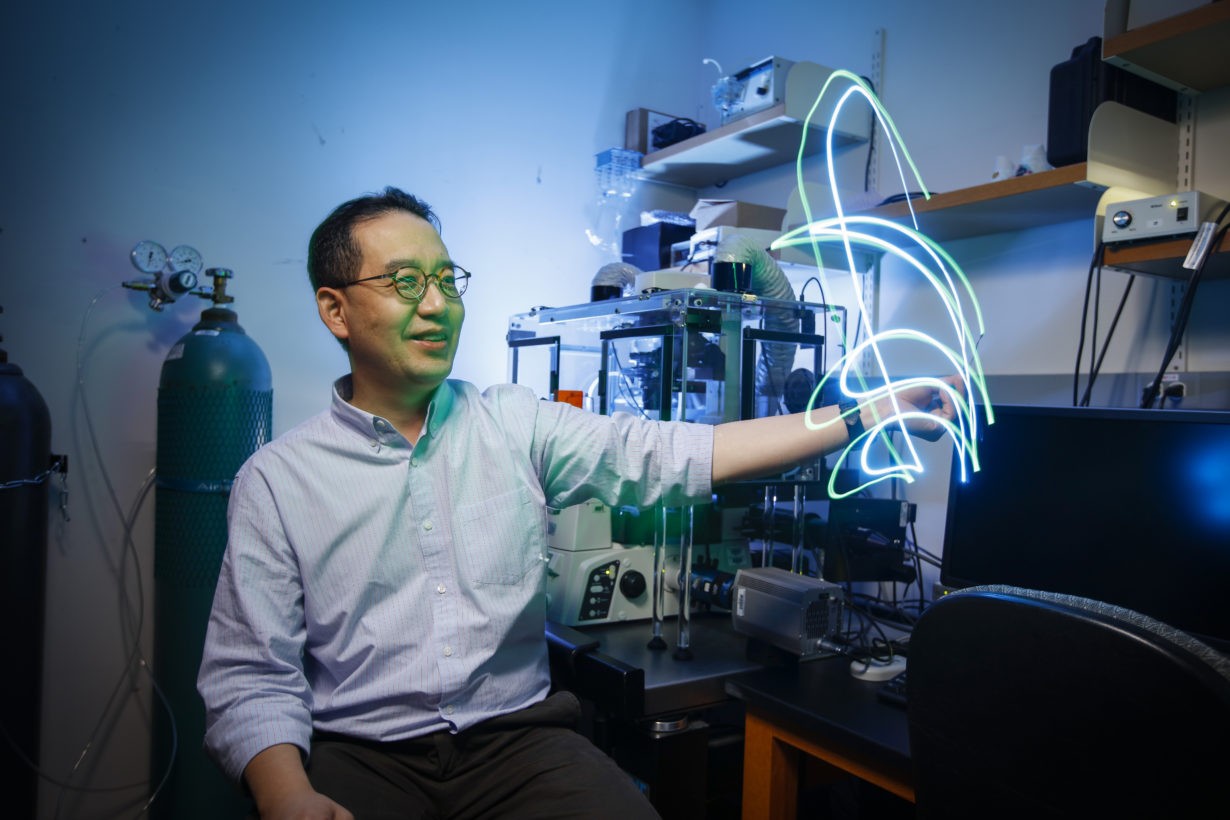 University of Rochester employee in lab moving pieces of fiber optic cable emitting streaks of blue and green light