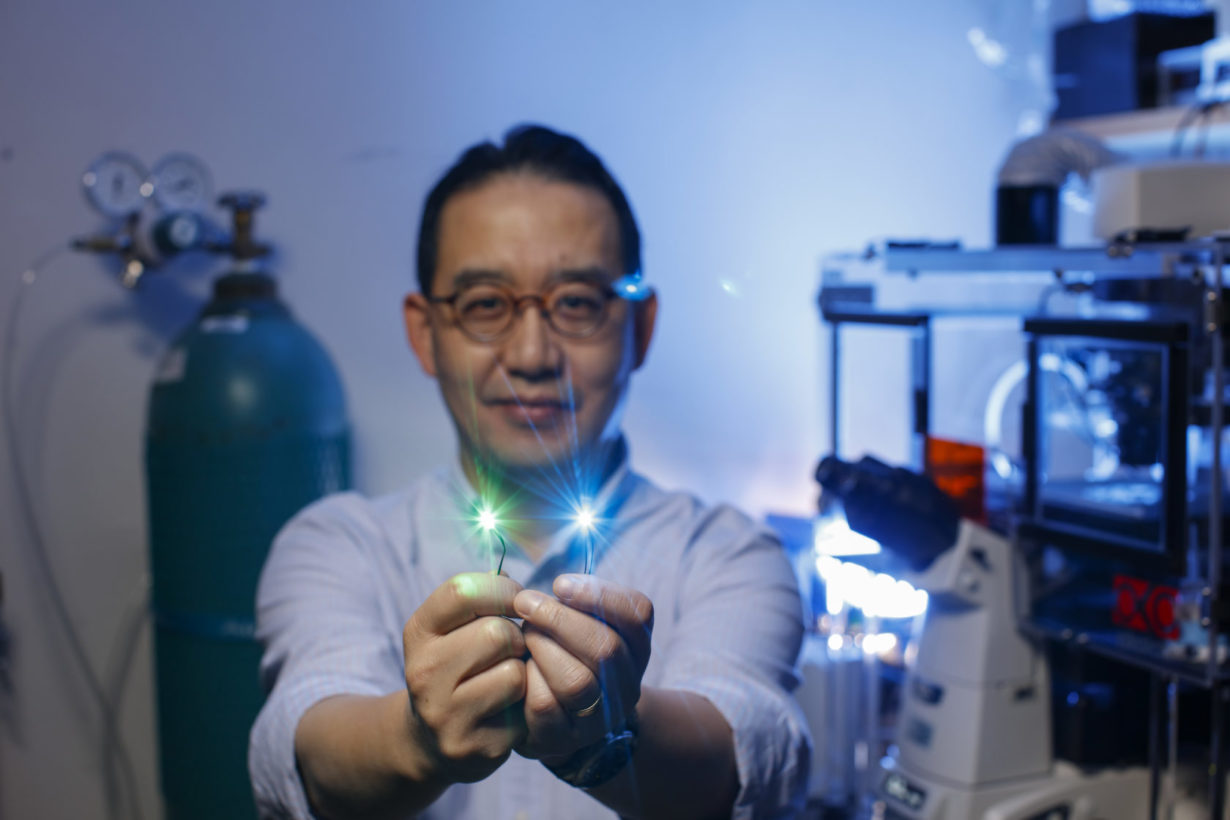 University of Rochester employee in lab holding pieces of fiber optic cable emitting blue and green light from the ends