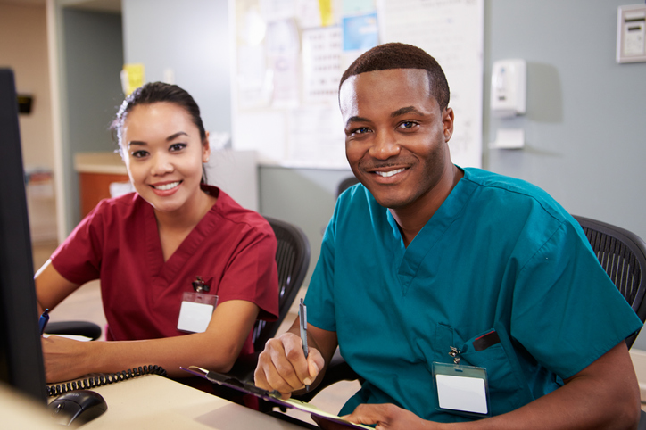 Male And Female Outpatient Access Specialist Working At Computer Station Smiling At Camera
