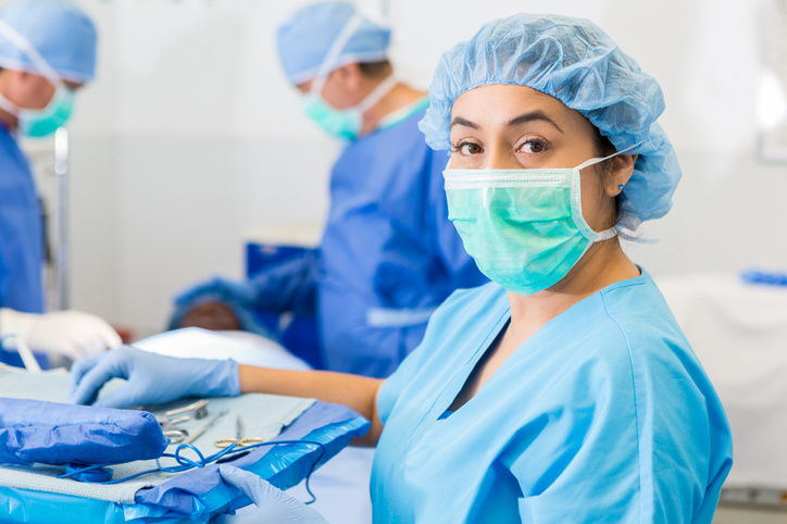 Hispanic surgical nurse or technician assisting with surgery in hospital