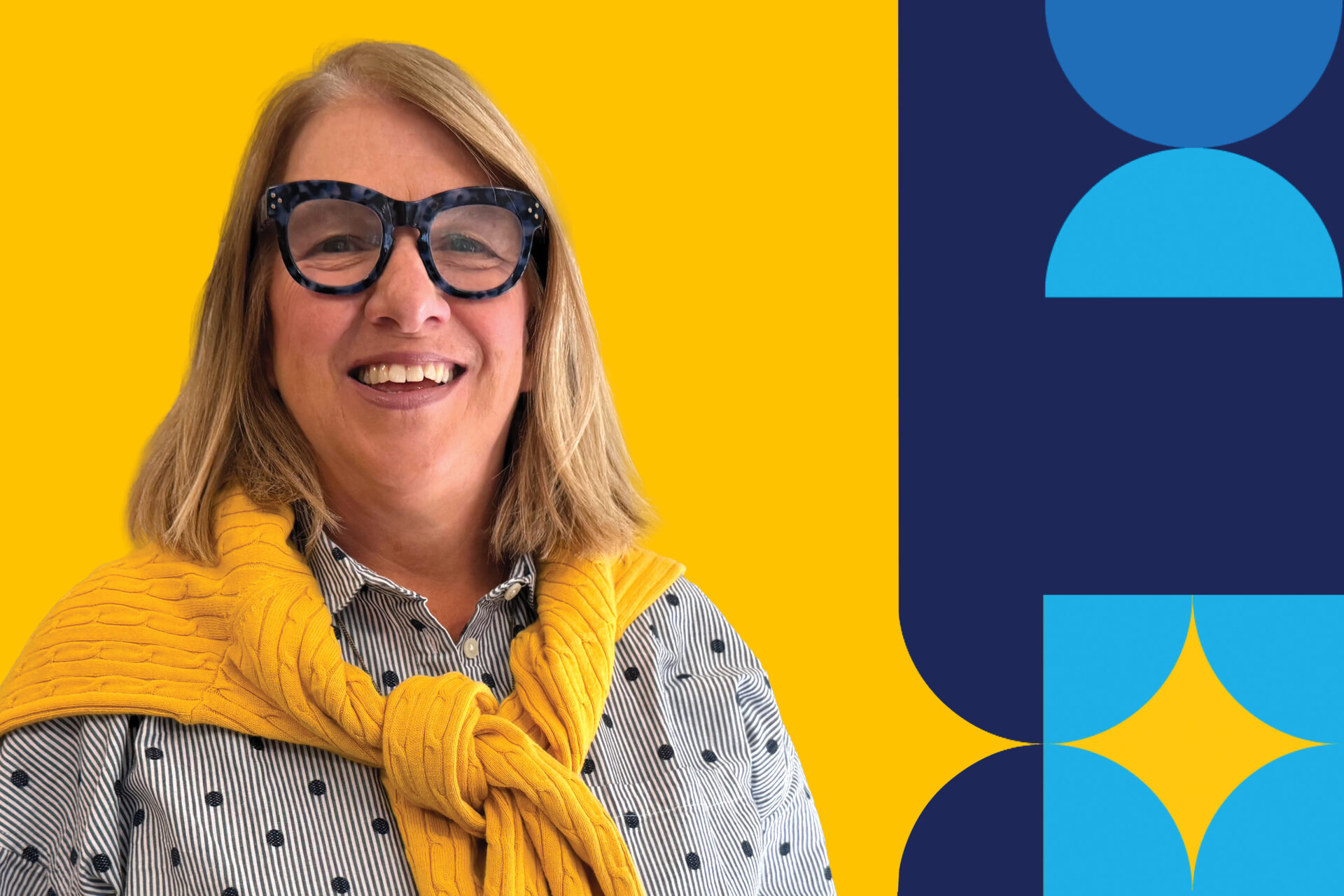 A woman named, Kathy Buckwell, wearing a black pair of glasses, smiling brightly with a yellow sweater drapped over her shoulders.