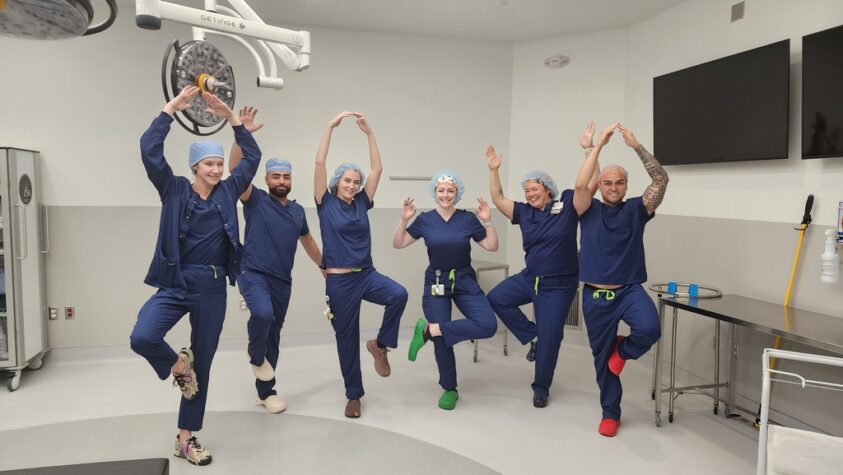 Six nurses are striking a balancing pose in an operating room.